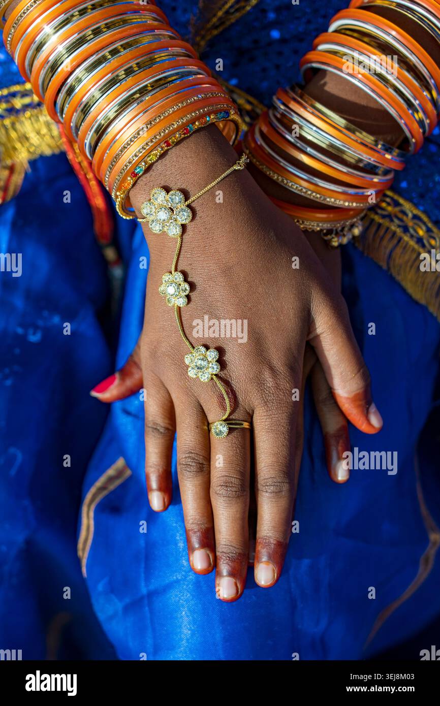 Indische Brauthände mit traditionellen orangen Armreifen und Goldschmuck. Nahaufnahme einer Frauenhände mit Henna-Orange und goldenen Metallarmbändern und Stockfoto