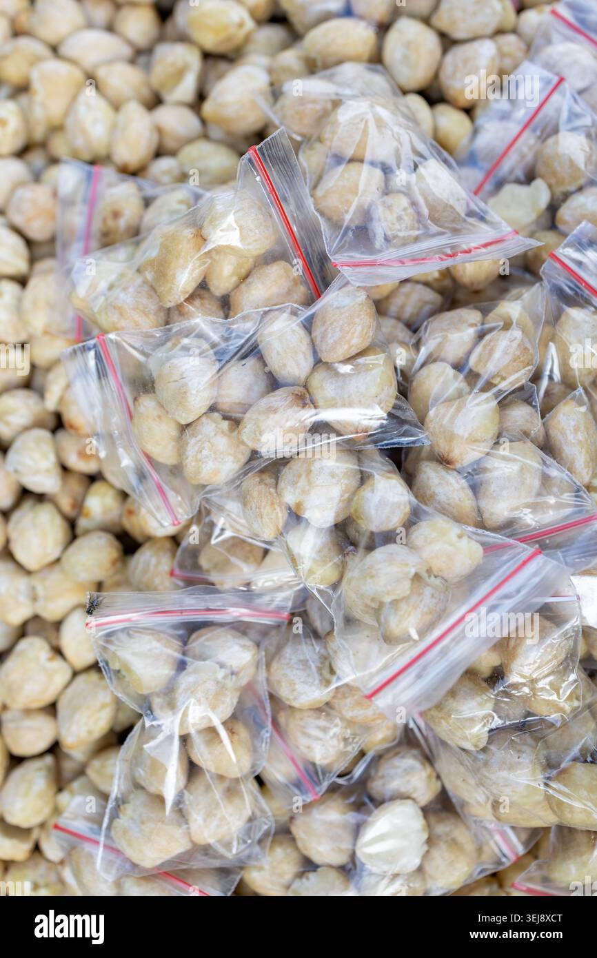 Geschälte Kerzennüsse in kleinen Plastikbeuteln mit Reißverschluss auf einem lokalen Markt. Rohe organische asiatische Gewürznüsse Haufen, Lebensmitteleinzelhandel Hintergrund. Stockfoto