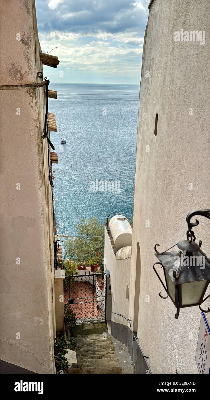 Malerischer Blick durch eine enge Straße in Positano, Italien, mit traditionellen Gebäuden, Vintage-Laterne und einem Blick auf den Strand und das türkisfarbene Meer Stockfoto