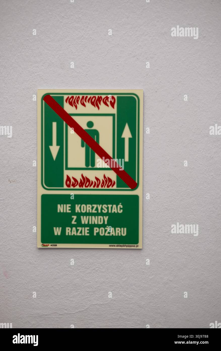Ein grün-weißes poliertes Brandschutzschild mit einer roten Diagonallinie über einem Aufzugssymbol ist an einer strukturierten weißen Wand in einer Inneneinrichtung angebracht. Stockfoto