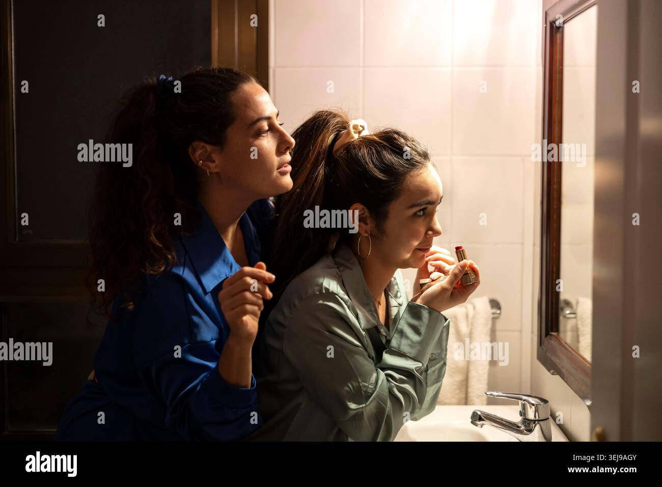 Junge Frauen im Pyjama schminken sich und teilen intime Momente in einem modernen Badezimmer Stockfoto