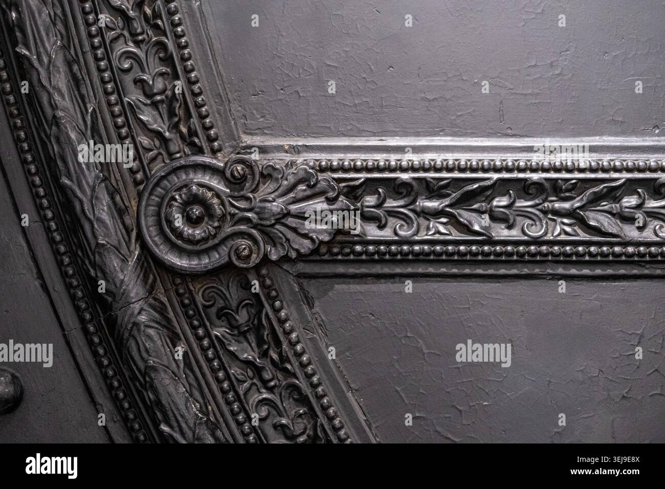 Dekorative architektonische Details aus Gusseisen sind in einer industriellen Umgebung auf einer dunkel lackierten Metalloberfläche montiert. Stockfoto