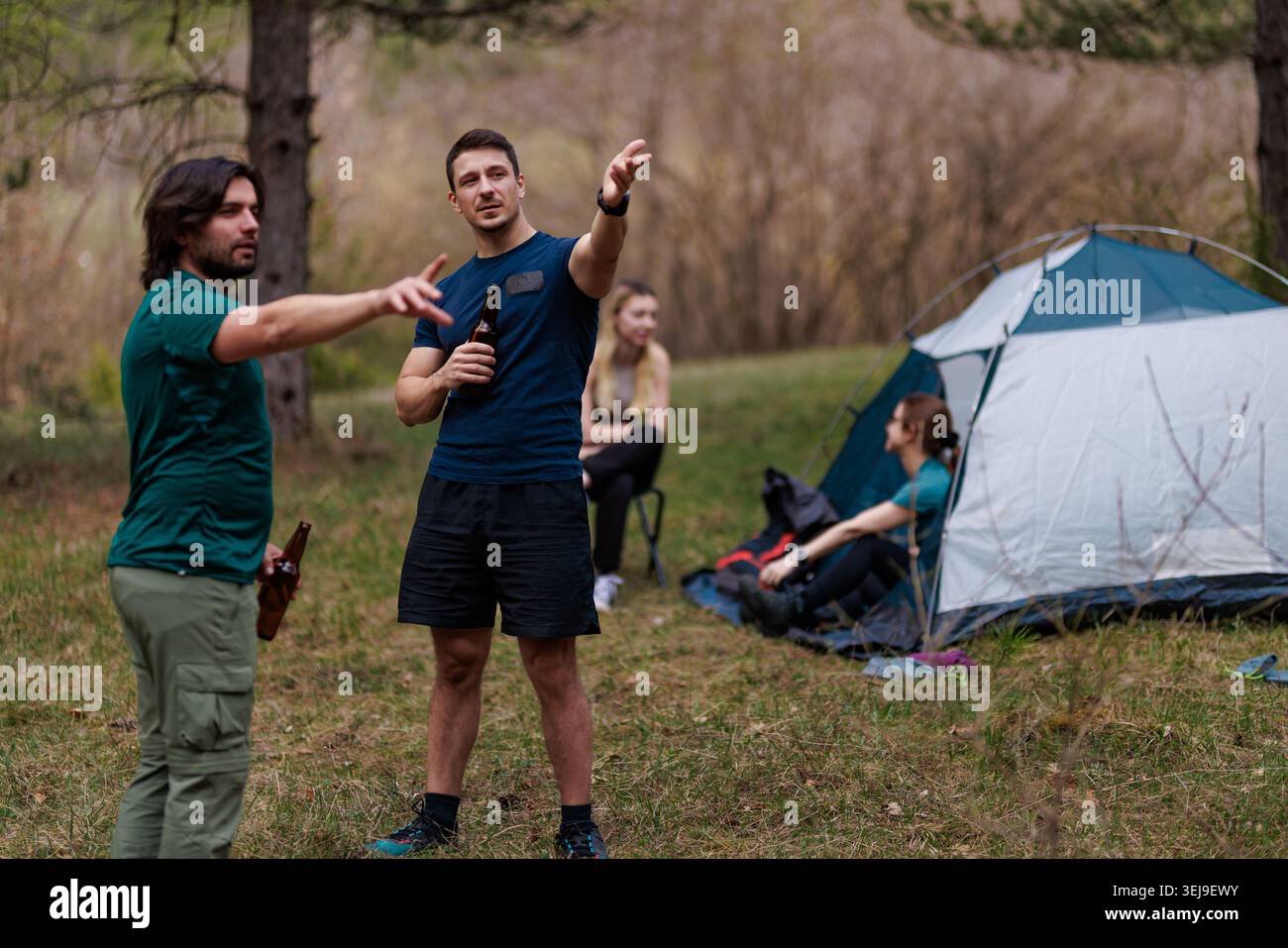 Freunde genießen es, gemeinsam in der Natur zu campen, während sie an einem sonnigen Tag im Wald Pläne in der Nähe ihres Zeltes besprechen Stockfoto