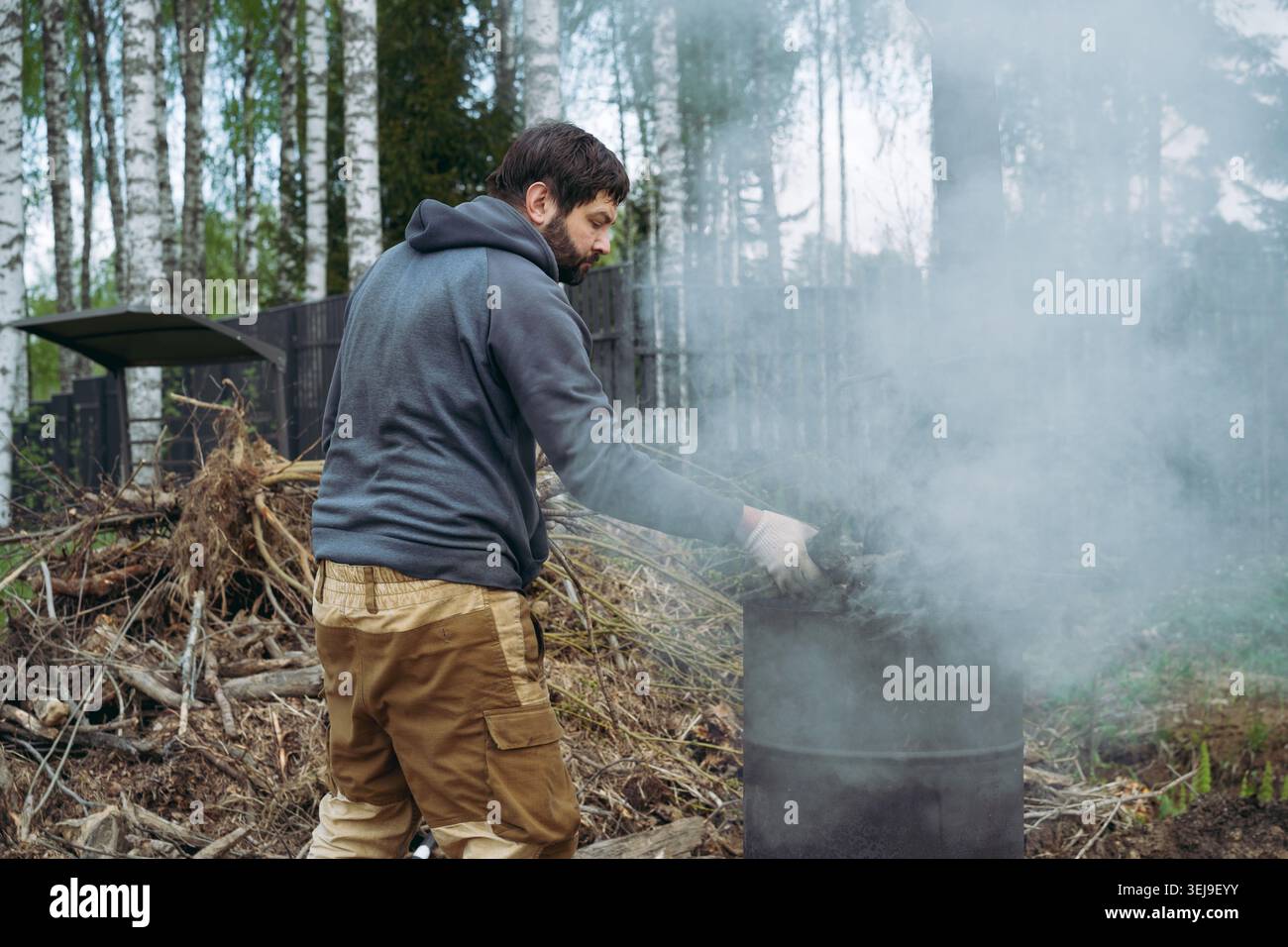 Ein Mann verbrennt Äste und Gartenabfälle in einem Metallfass auf seinem Landgrundstück. Stockfoto