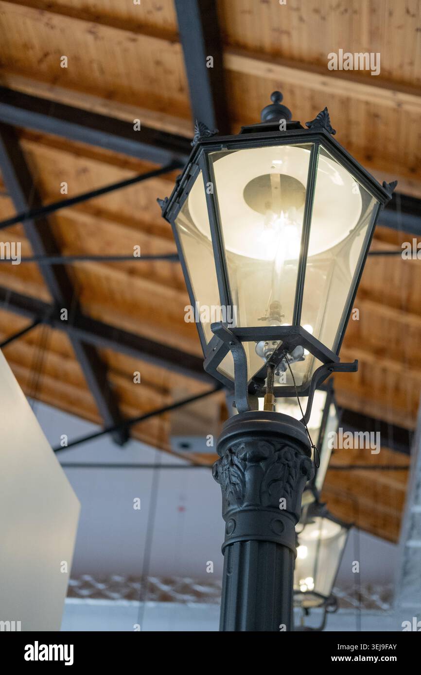 Eine beleuchtete Laterne aus schwarzem Metall im Vintage-Stil steht unter einer Holzlattendecke in einem Innenbereich. Stockfoto