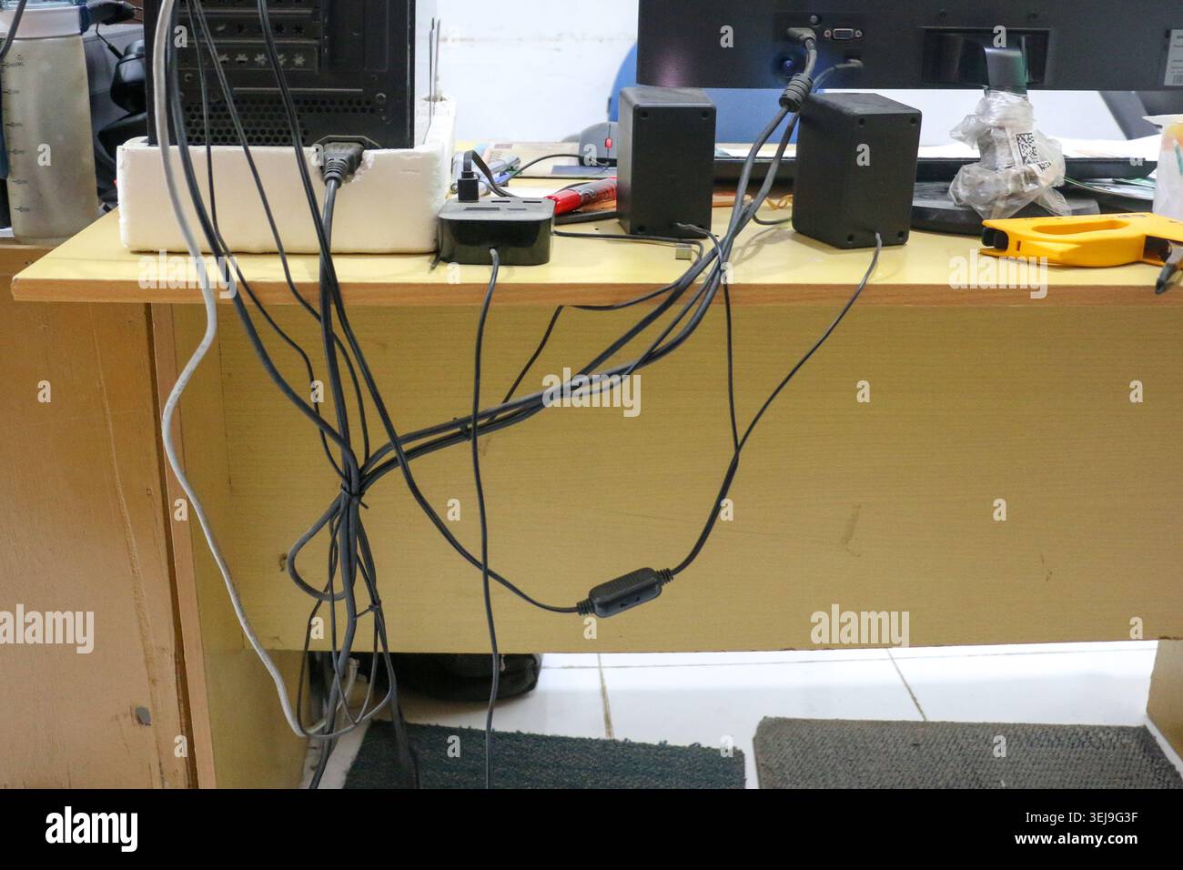 Unordentlicher Computertisch mit verwickelten Kabeln und elektronischen Geräten in Office Workspace Stockfoto