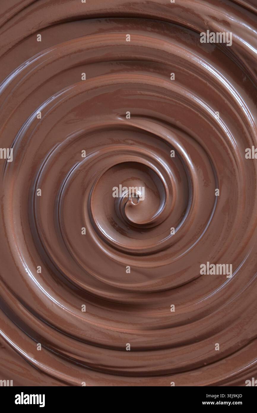 Nahaufnahme einer glänzenden flüssigen Milchschokolade, die sich in einer glatten Spirale dreht und eine reichhaltige und cremige geschmolzene Schokoladentextur zeigt. Stockfoto