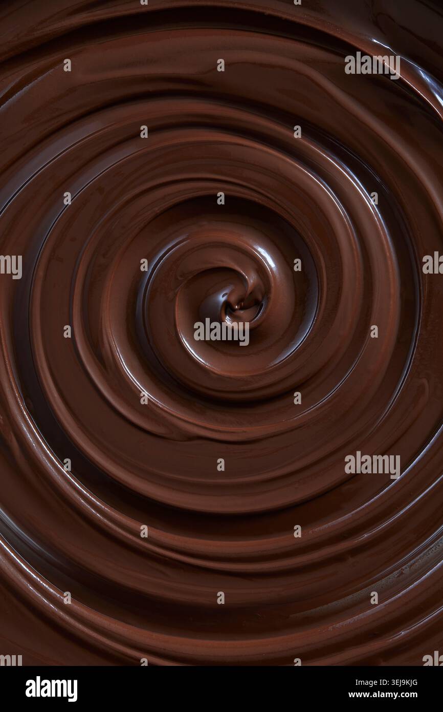 Glatte, glänzende, flüssige dunkle Schokolade, die in einer kräftigen Spirale wirbelt und in Nahaufnahme eine luxuriöse Textur aus geschmolzener Schokolade zeigt. Stockfoto