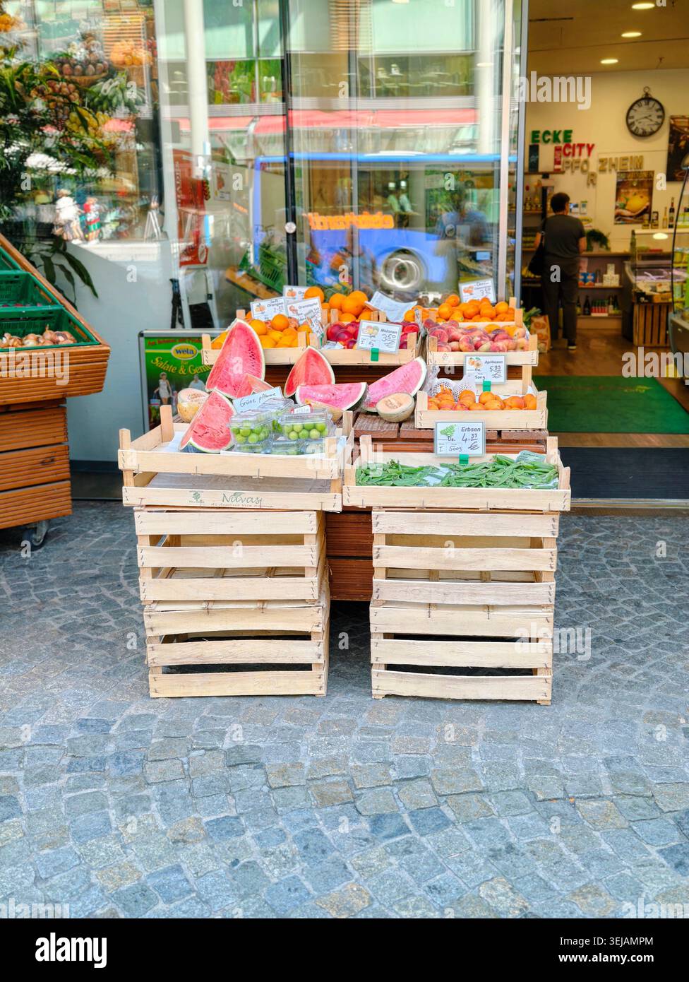 PFORZHEIM, DEUTSCHLAND - 28. MAI 2026 Wassermelonen, Orangen und frisches Obst in Holzkisten auf einer Straßenausstellung vor einem lokalen Supermarkt mar Stockfoto