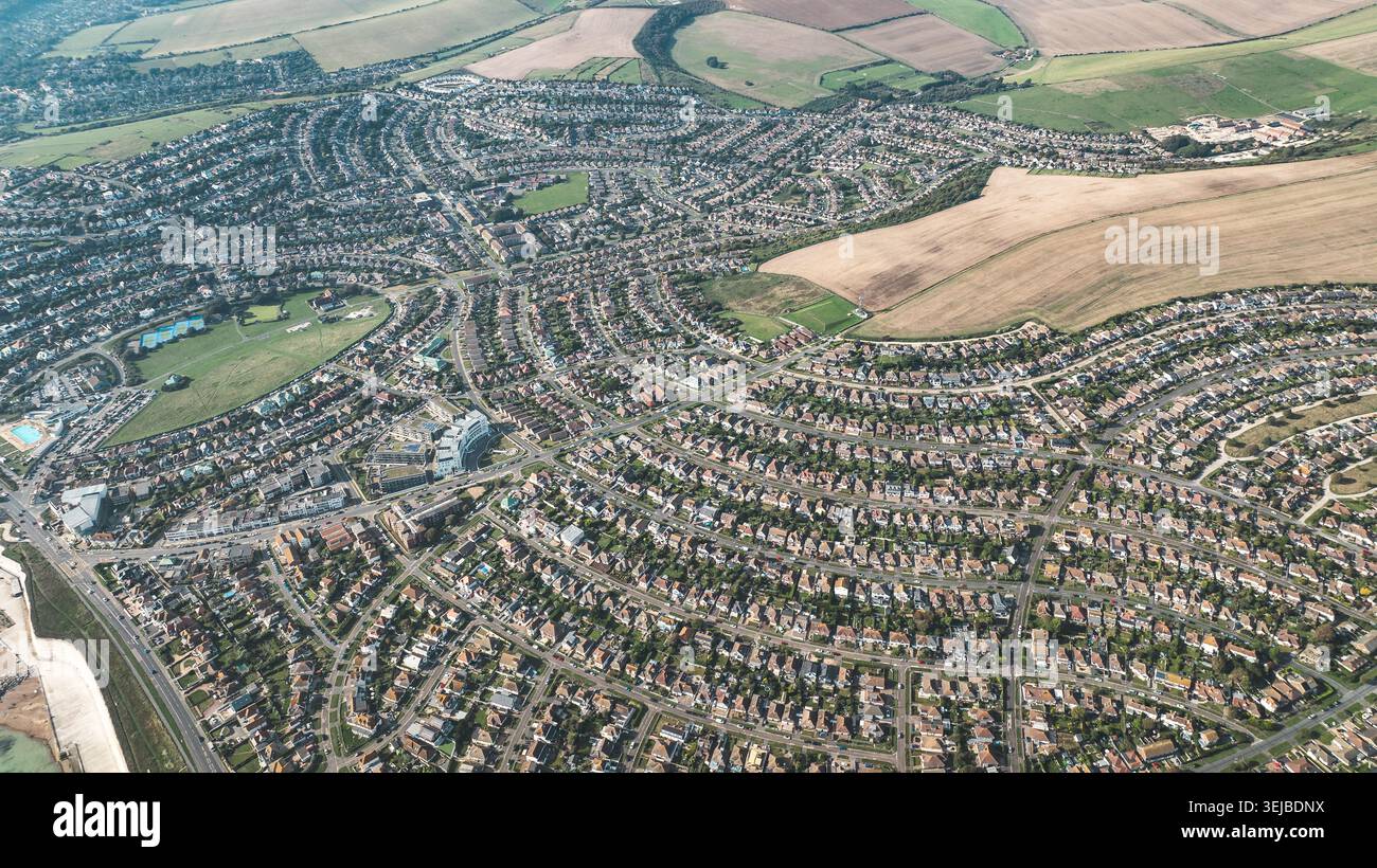 Eine weitläufige Luftperspektive zeigt ein dicht besiedeltes Wohngebiet mit kurvenreichen Straßen und zahlreichen Häusern, die von landwirtschaftlichen Flächen begrenzt werden Stockfoto