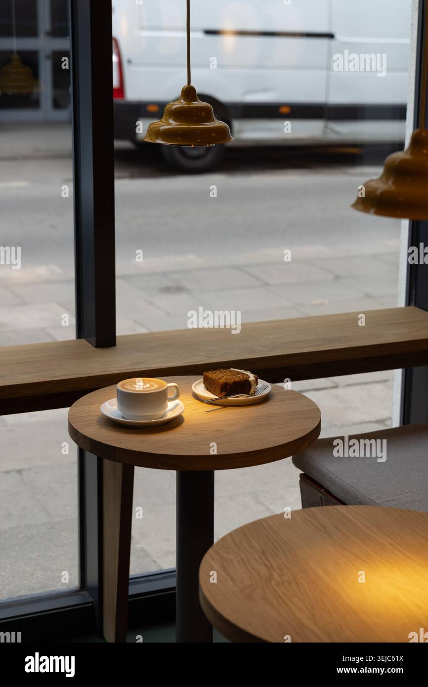 Kaffee und Kuchen in einem modernen Café-Interieur am Fenster, Fernarbeit Stockfoto
