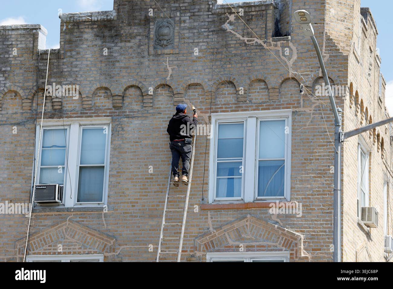 Ein Arbeiter an einer Verlängerungsleiter deckt Risse in einer Mauermauer eines New Yorker Gebäudes mit Epoxid ab. Stockfoto