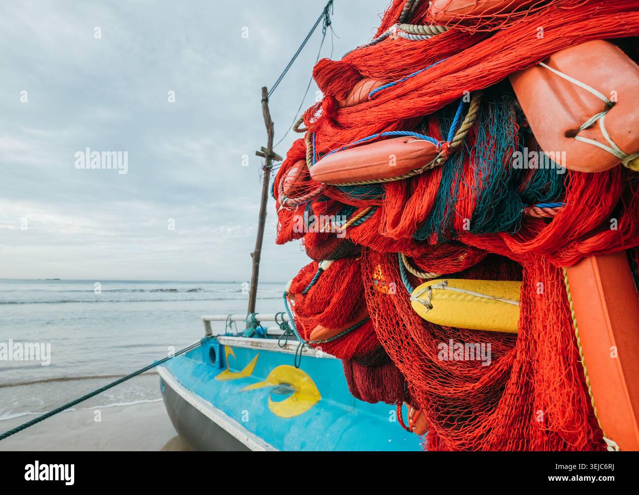 Aus nächster Nähe sehen Sie lebendige rote Fischernetze mit farbenfrohen Plastikwagen, die auf einem traditionellen Sri-lankischen Auslegerboot am Sandstrand am Meer geparkt sind Stockfoto