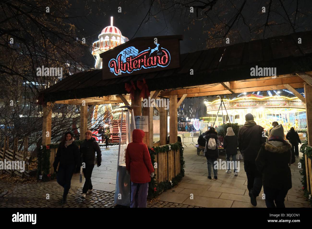 Oslo, Norwegen-25. November 2025: Touristen gehen nachts am hölzernen Eingangstor des Weihnachtsmarktes Jul i Vinterland in Oslo, Norwegen vorbei. Stockfoto