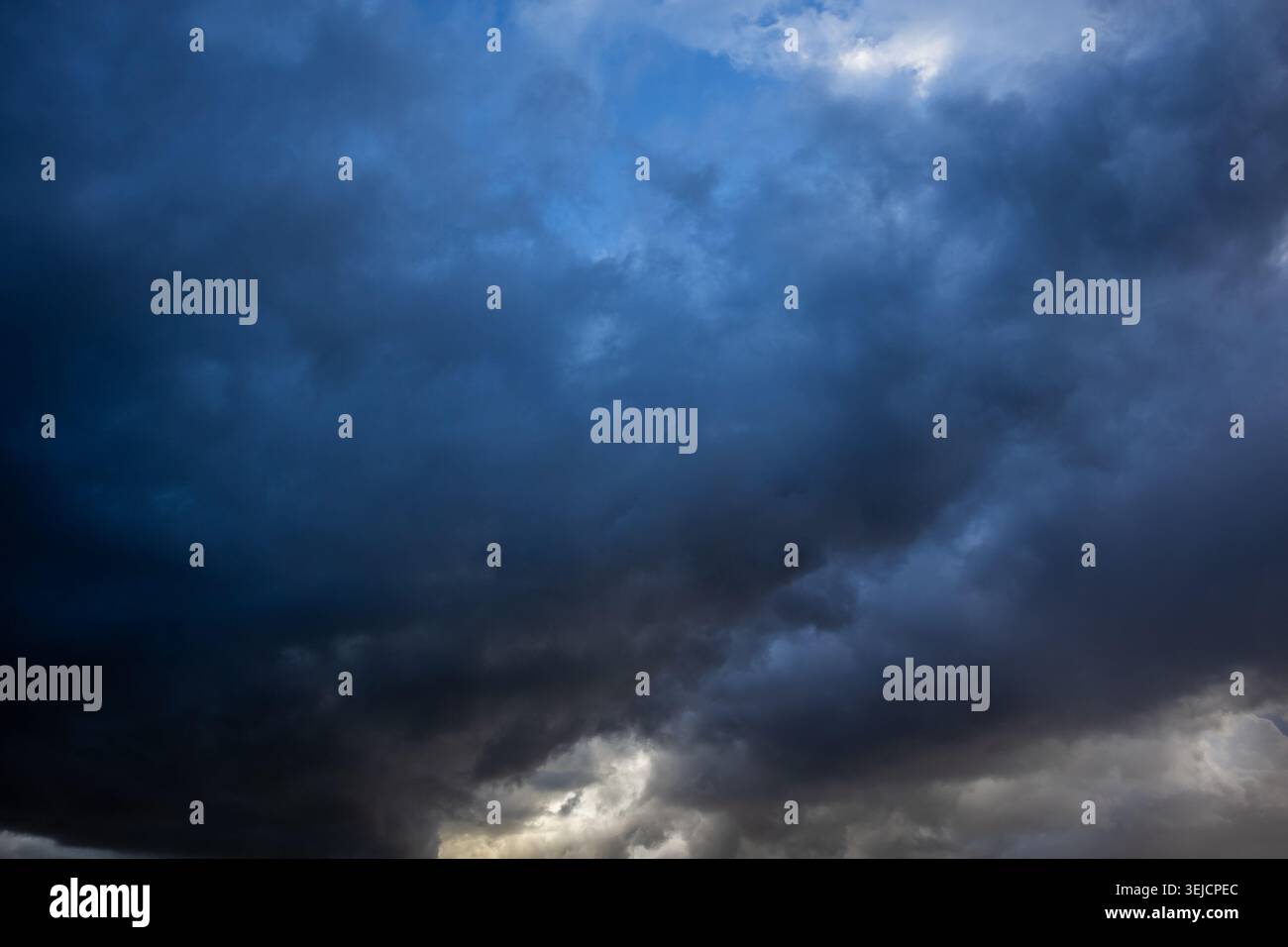 Dramatische dunkle Sturmwolken mit einem Lichtbruch unten vor einem tiefblauen Himmel Stockfoto