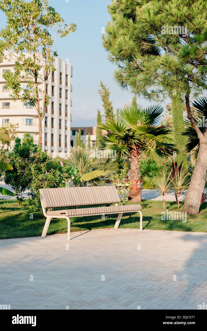 Moderne Parkbank umgeben von Palmen und üppigem Grün in städtischem Wohngebiet. Stockfoto