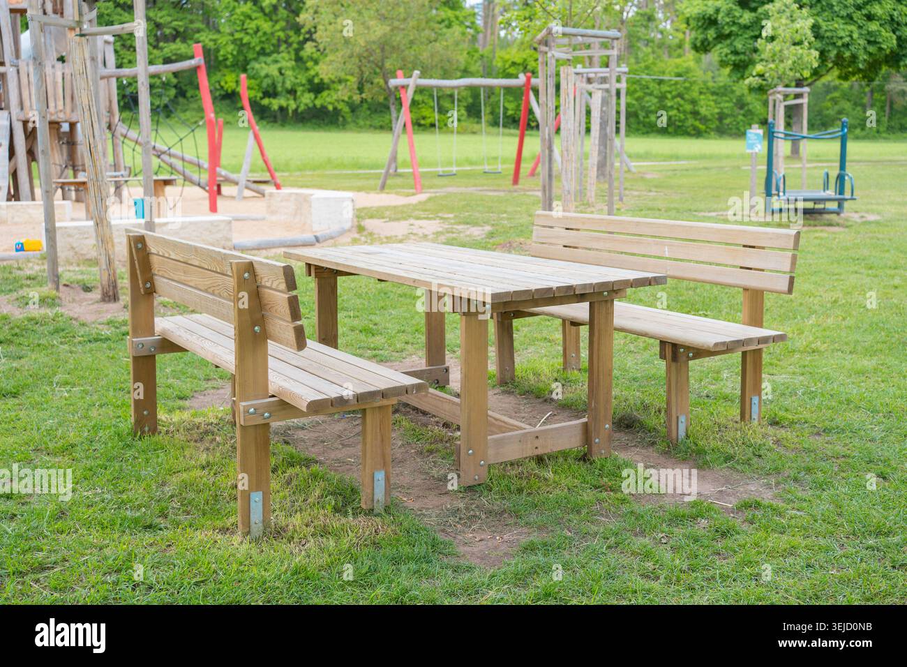 Ein leerer rustikaler Picknicktisch aus Holz, integriert mit Bänken, die auf einem grünen Rasen in einem öffentlichen Park stehen. Der perfekte Ort für Stockfoto