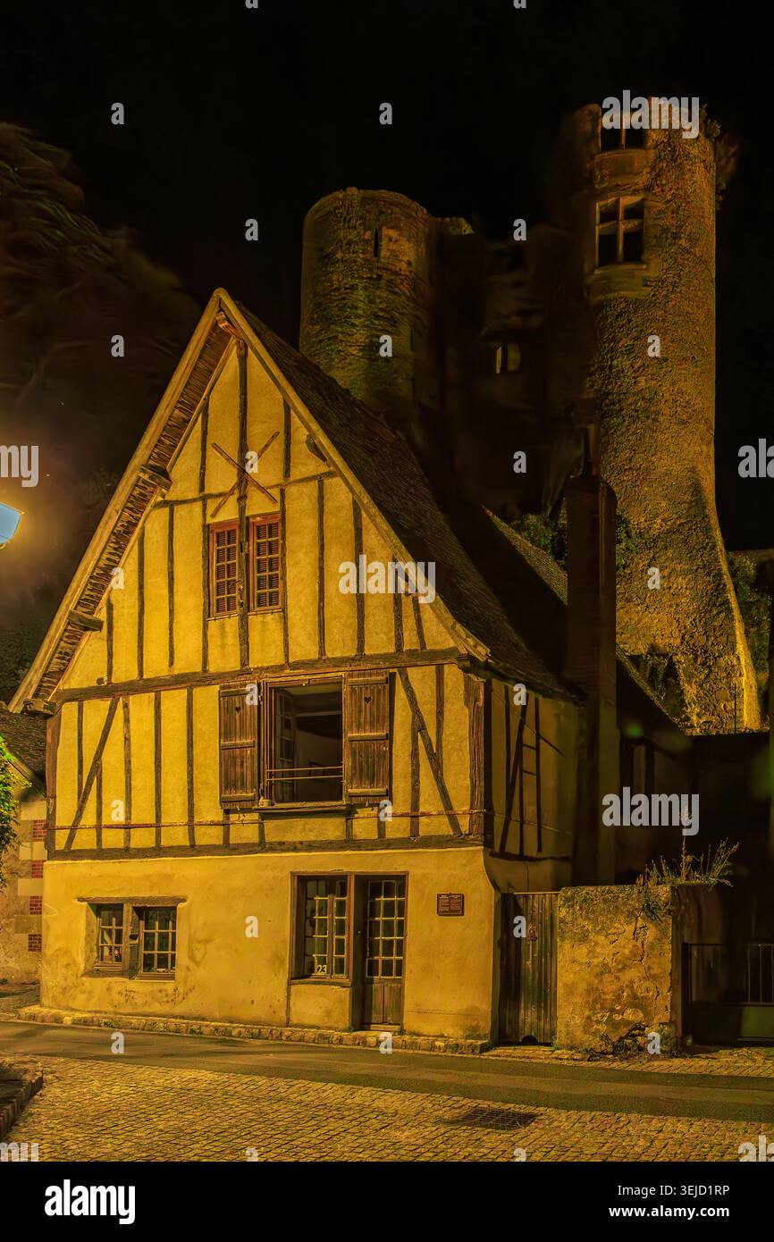 Montrésor, Frankreich - 21.08.2023: Historisches Fachwerkhaus und Efeu-bekleideter Steinturm, der unter warmer Nachtbeleuchtung leuchtet Stockfoto