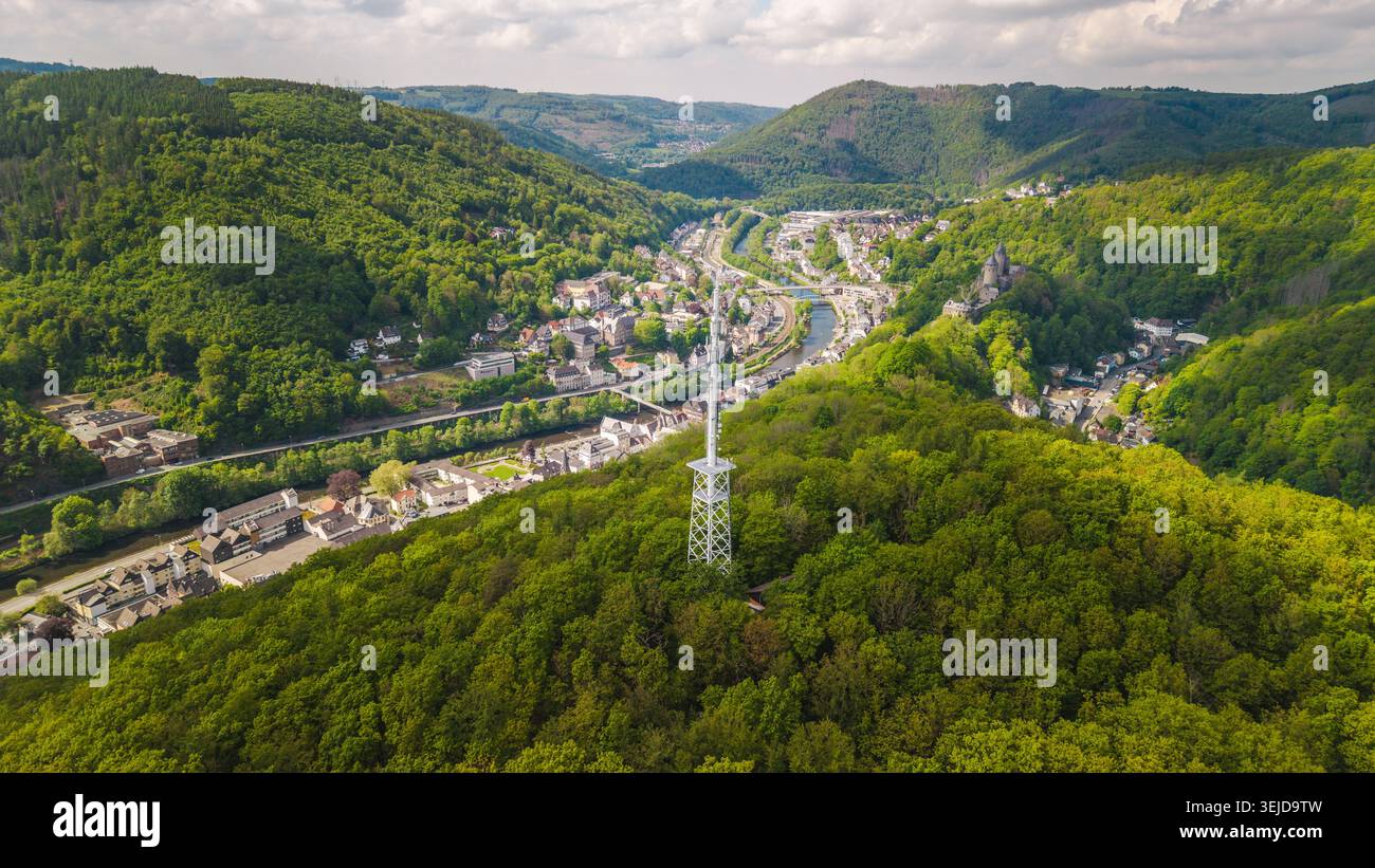 Aus der Vogelperspektive auf den Kommunikationsturm über dem bewaldeten Tal und die kleine deutsche Stadt mit Fluss und Hügeln unter bewölktem Himmel Stockfoto