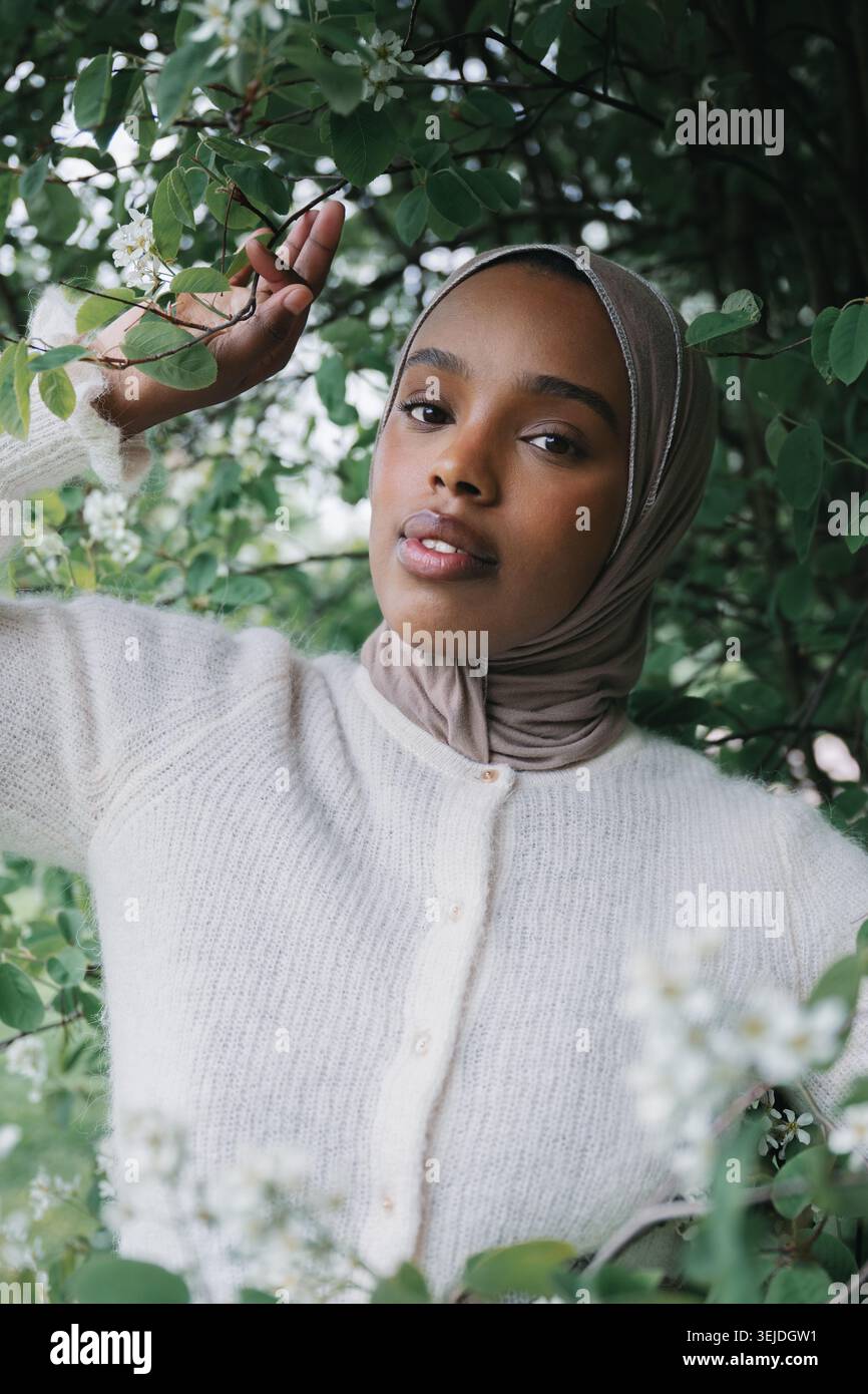 Junge muslimische Frau im Hijab zwischen blühenden Ästen im Frühlingspark Stockfoto