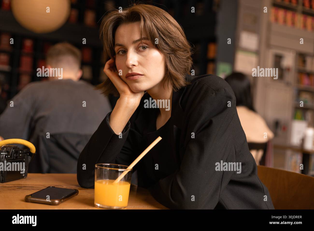 Eine junge Frau in Black Blazer am Cafe Table, die in die Kamera schaut Stockfoto