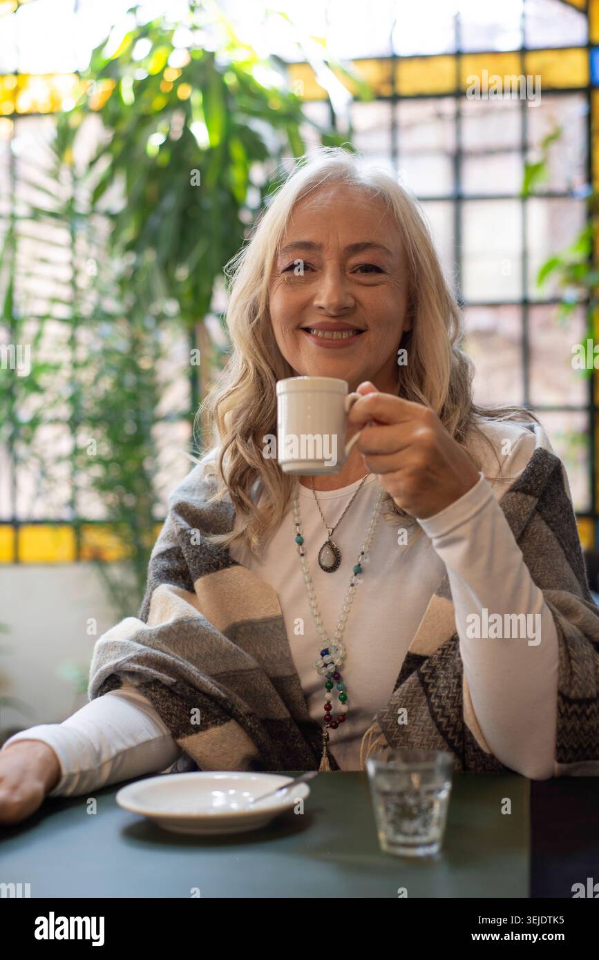 Lächelnde reife Frau, die in einem Café eine Tasse hält Stockfoto