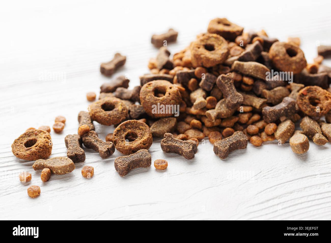 Trockenfutter für Hunde verschiedener Formen auf weißem Holzhintergrund. Stockfoto