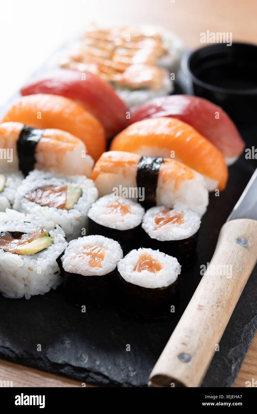 Verschiedene Sushi-Auswahl und Sojasauce auf Schiefertablett auf Holztisch Stockfoto