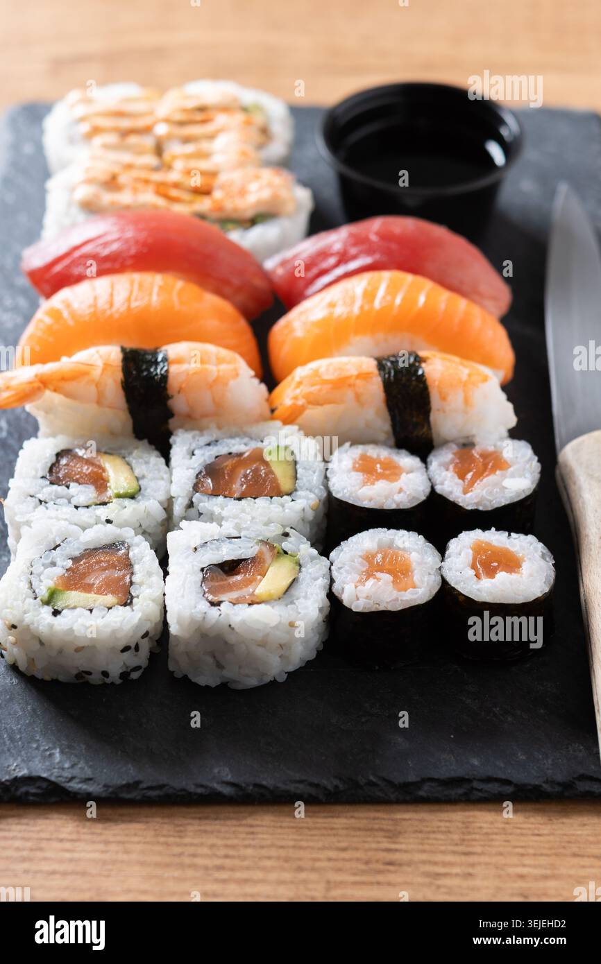 Verschiedene Sushi-Auswahl und Sojasauce auf Schiefertablett auf Holztisch Stockfoto