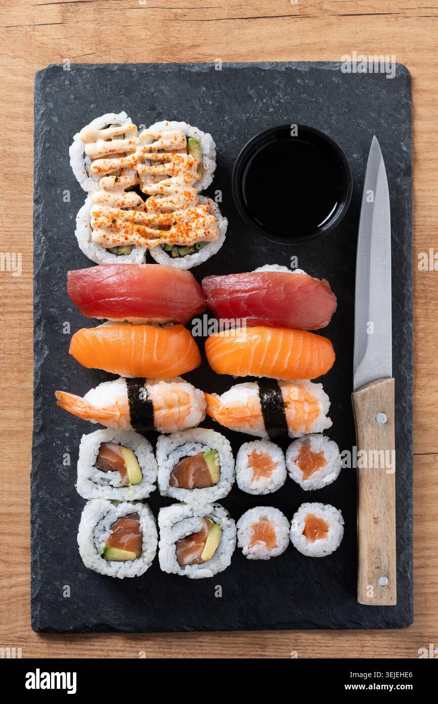 Verschiedene Sushi-Auswahl und Sojasauce auf Schiefertablett auf Holztisch Stockfoto