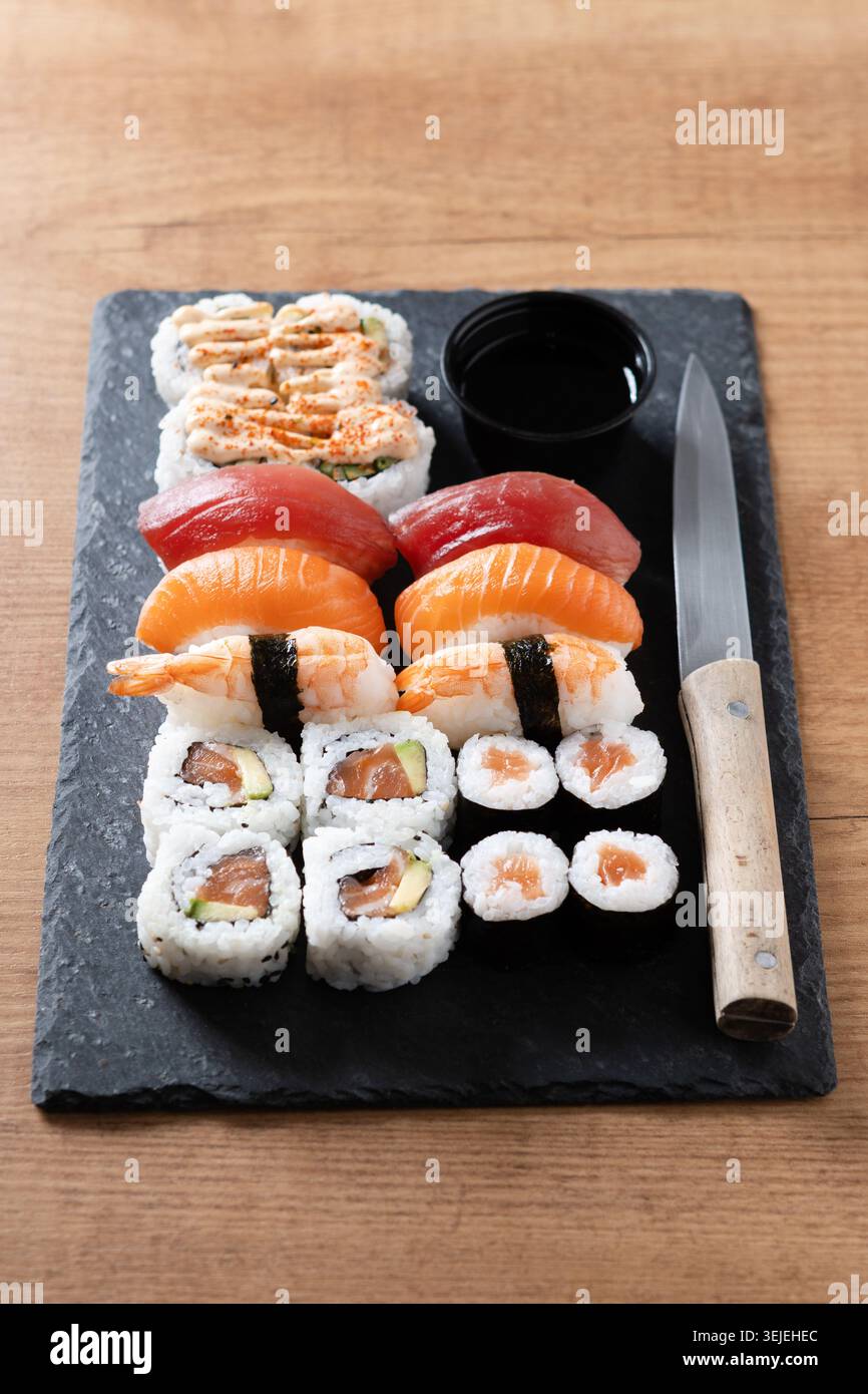 Verschiedene Sushi-Auswahl und Sojasauce auf Schiefertablett auf Holztisch Stockfoto