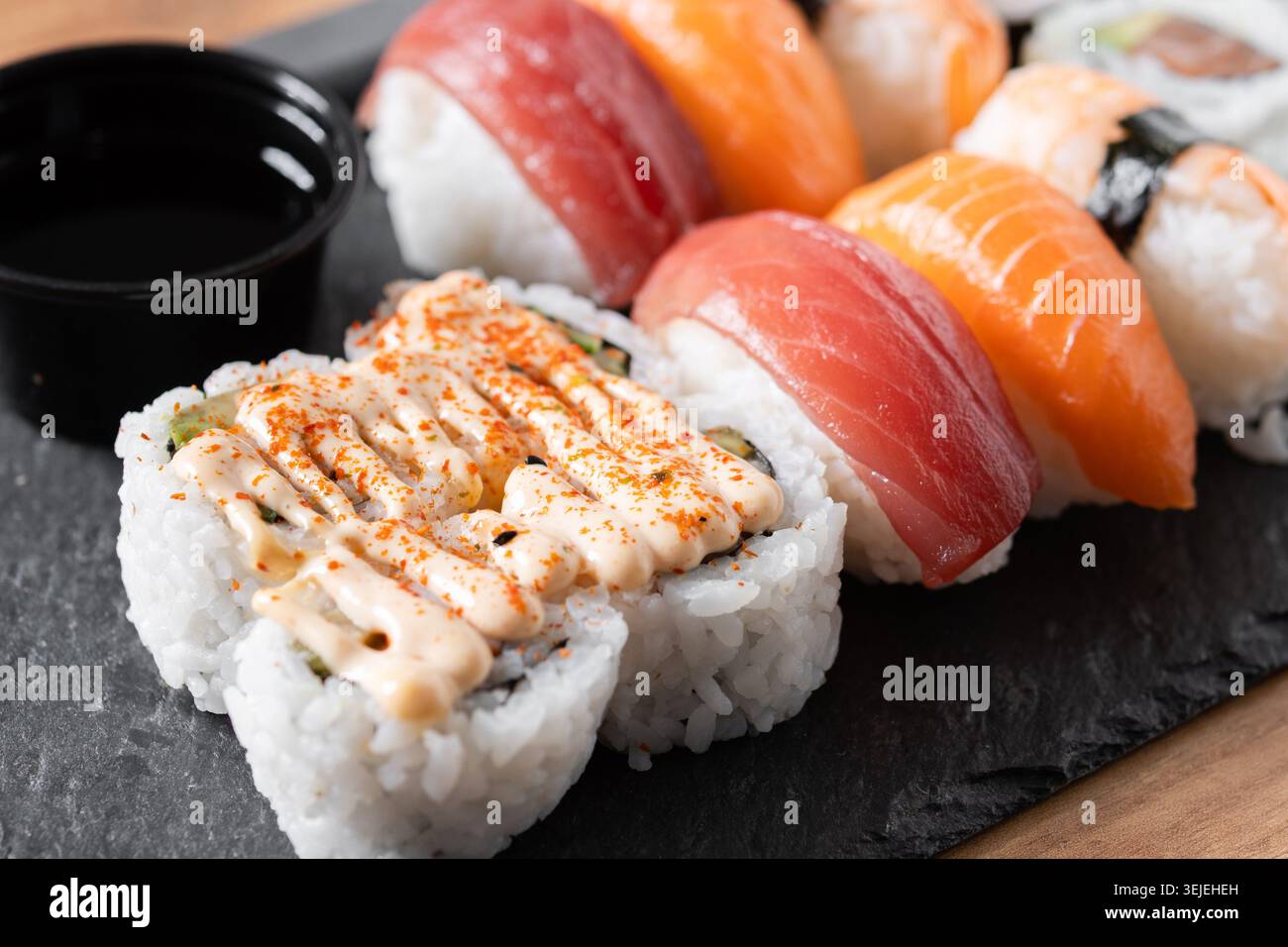 Verschiedene Sushi-Auswahl und Sojasauce auf Schiefertablett auf Holztisch Stockfoto