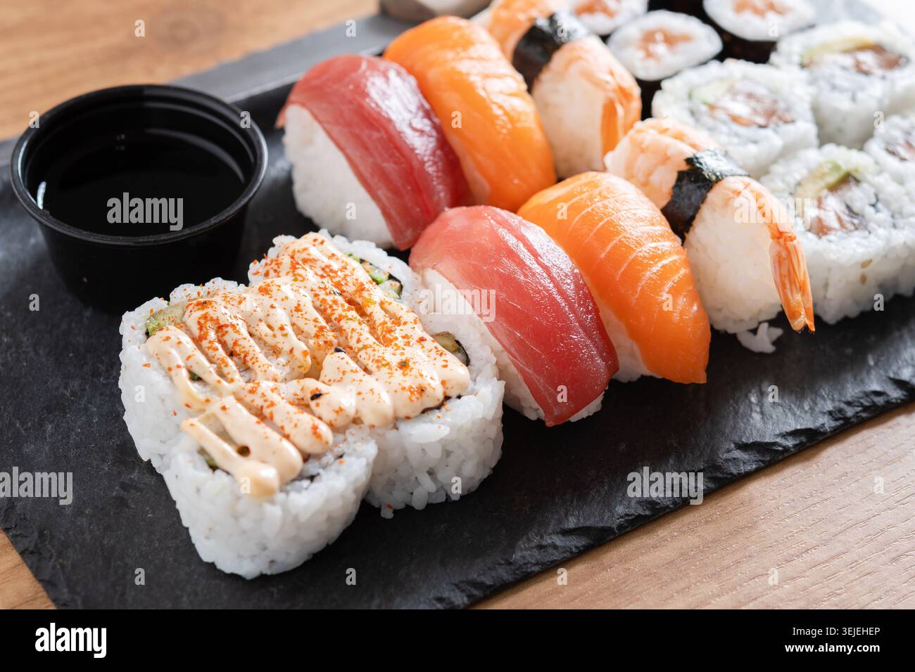 Verschiedene Sushi-Auswahl und Sojasauce auf Schiefertablett auf Holztisch Stockfoto