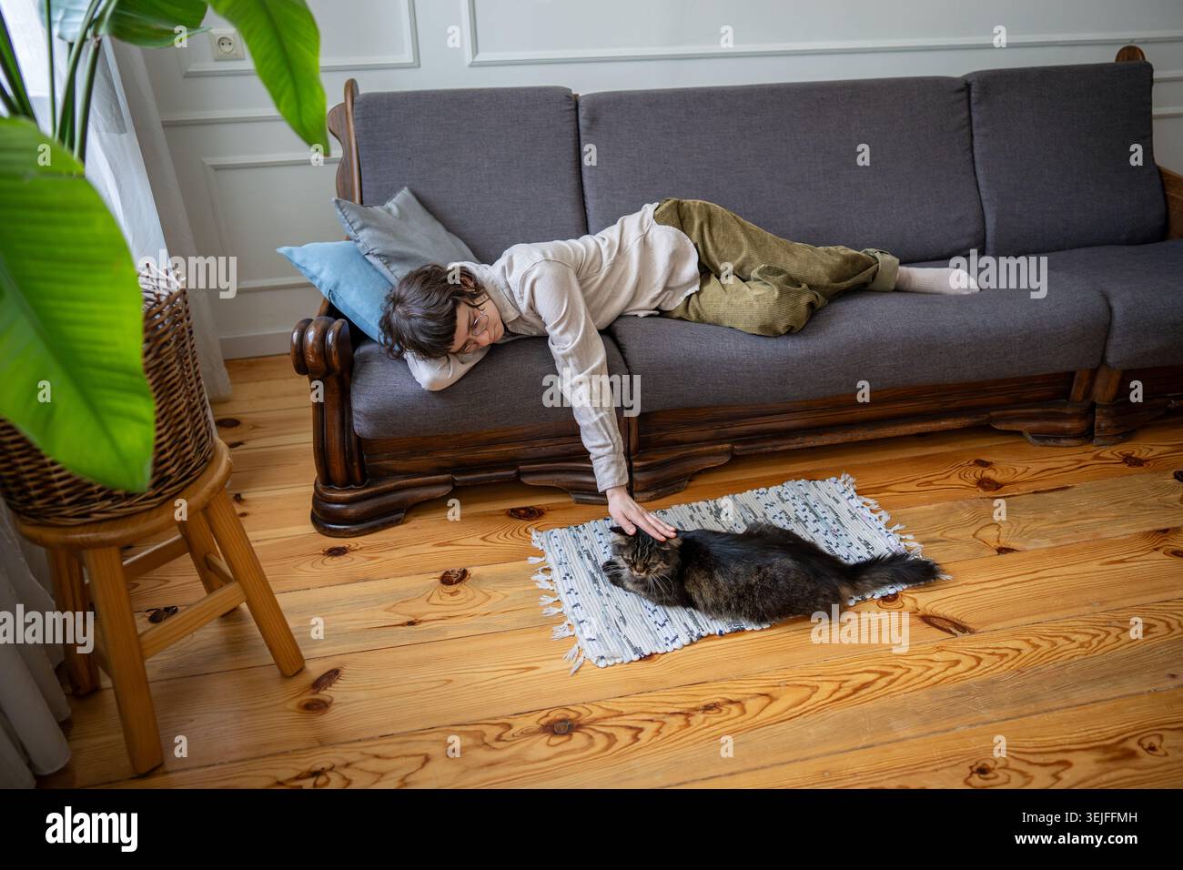 Müde Frau, die zu Hause ausruht und Katzenfreund streichelt, die neben der Couch auf weichem Teppich zu Hause liegt, langsames Leben Stockfoto