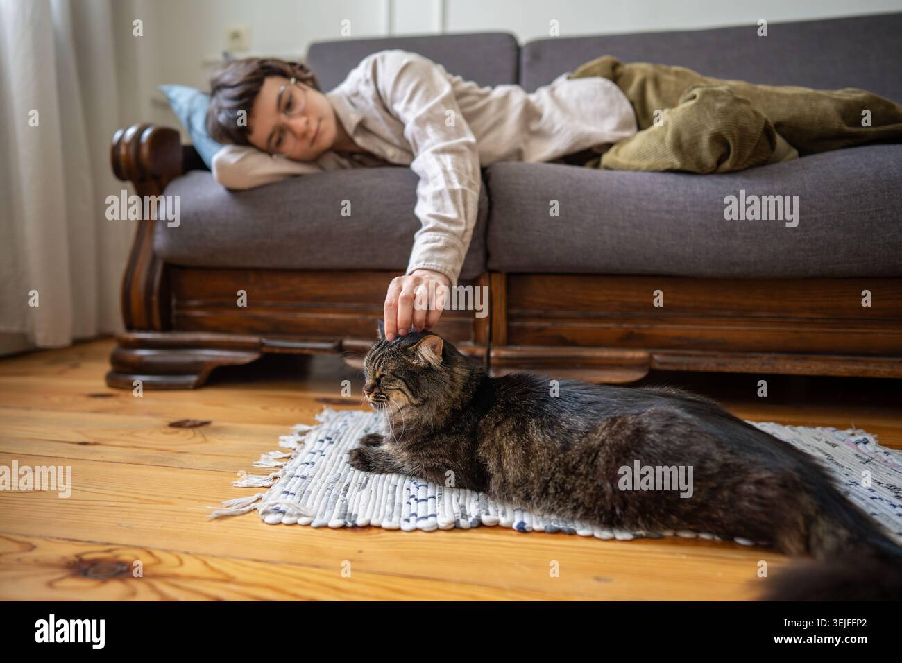 Müde Frau, die zu Hause ausruht und Katzenfreund streichelt, die neben der Couch auf weichem Teppich zu Hause liegt, langsames Leben Stockfoto