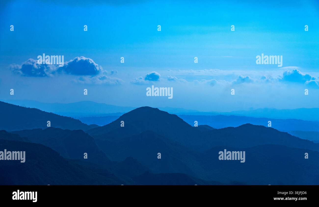 Mehrschichtige Bergkämme unter einem blauen Himmel mit verstreuten Wolken Stockfoto