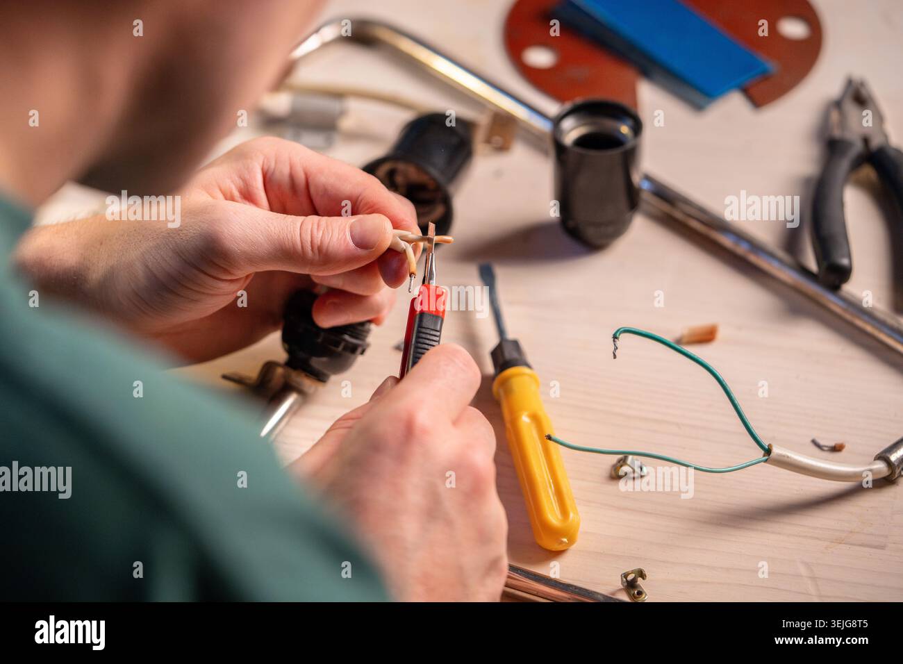 Handwerker, der in der Werkstatt arbeitet, um den Schutz des Kabelsystems der alten Lampe mit einem Messer zu reparieren. Stockfoto