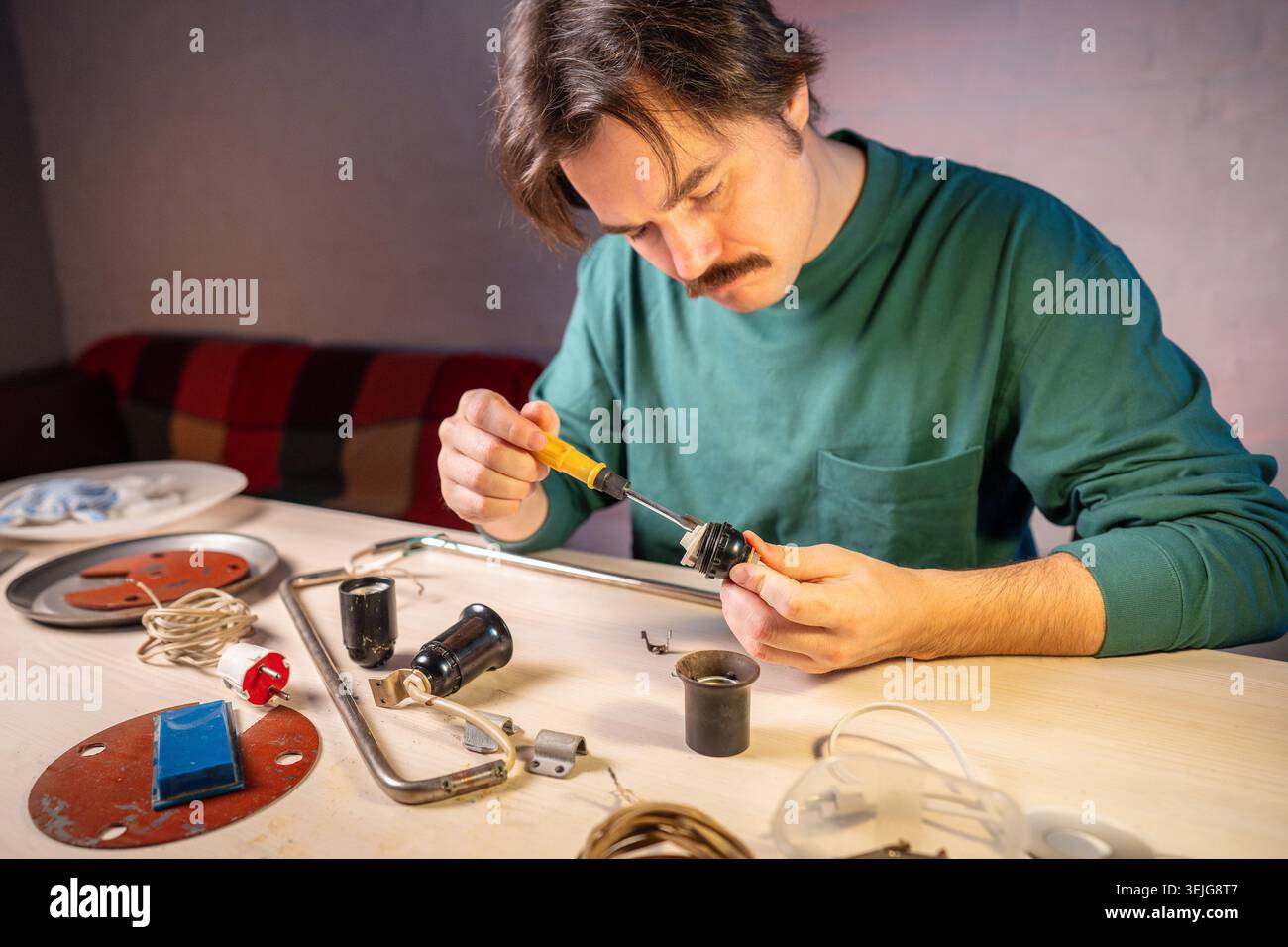 Handwerker in der Werkstatt, der mit Schraubendreher-Werkzeug Glühlampensockel Teile von Vintage-Lampe ausschraubt. Stockfoto