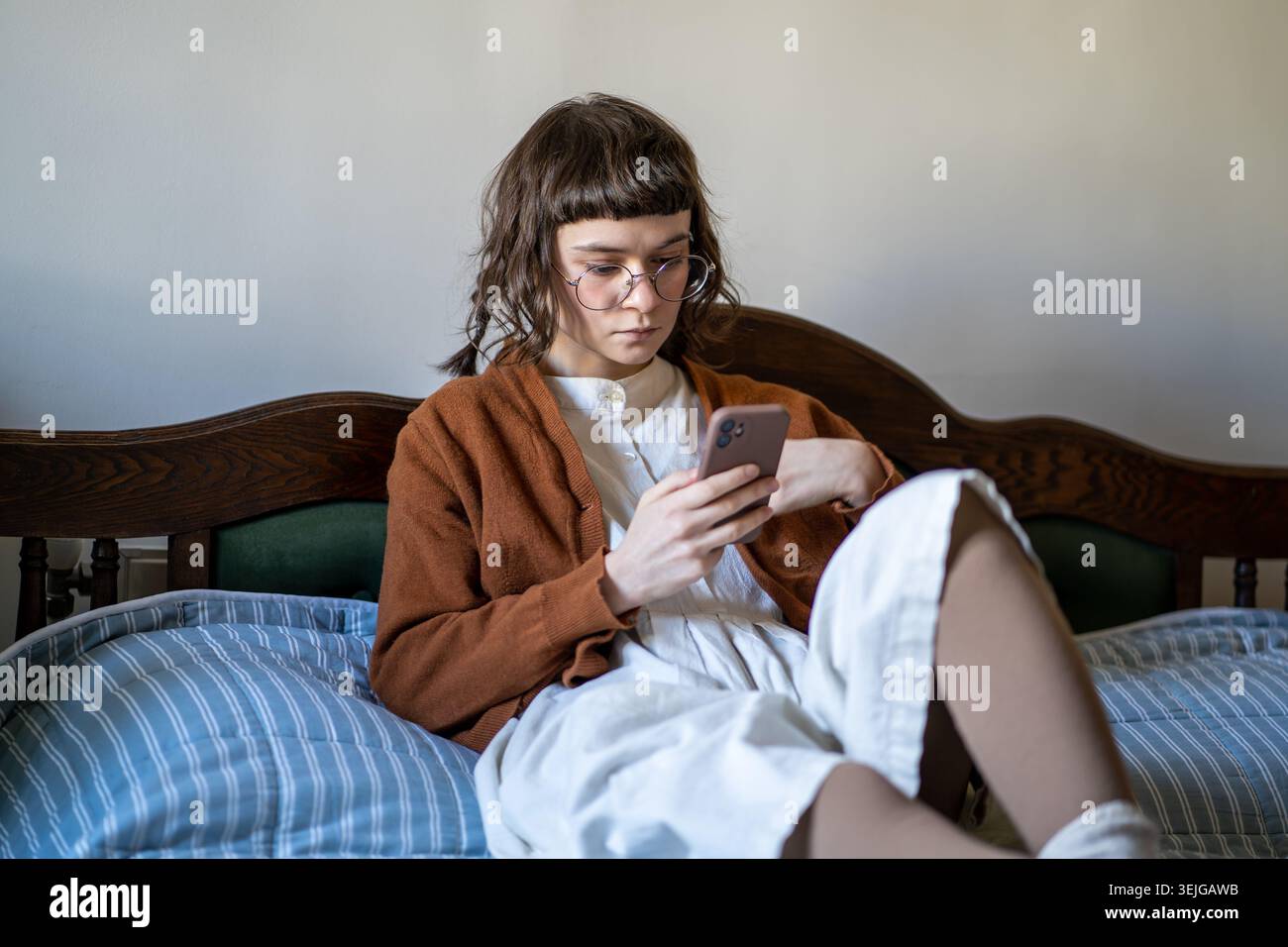 Nachdenkliches Hipster-Mädchen in Brille, das im Vintage-Stil aussehende Smartphone-Bildschirm trägt und Informationen liest. Stockfoto