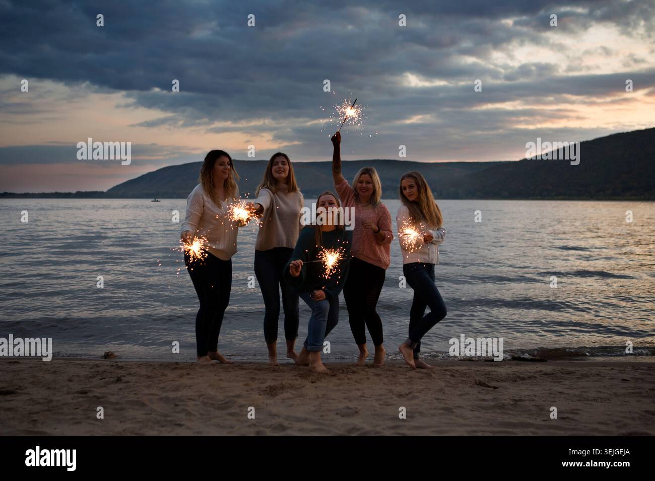 Gruppe glückliche Freunde, die am Strand mit Wunderkerzen feiern. Erwachsenencamp, Wellness-Rückzugsort, Outdoor-Aktivitäten, Stockfoto