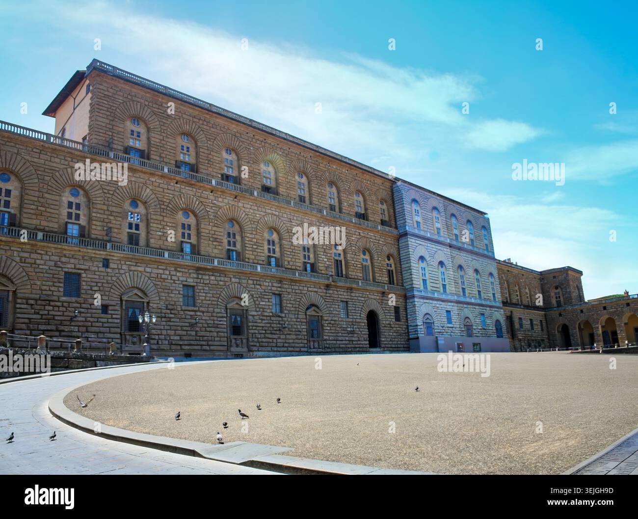 Die massive rustikale Steinfassade des Palazzo Pitti steht vor einem offenen, schrägen Platz unter einem hellblauen Himmel in Florenz, Italien. Stockfoto