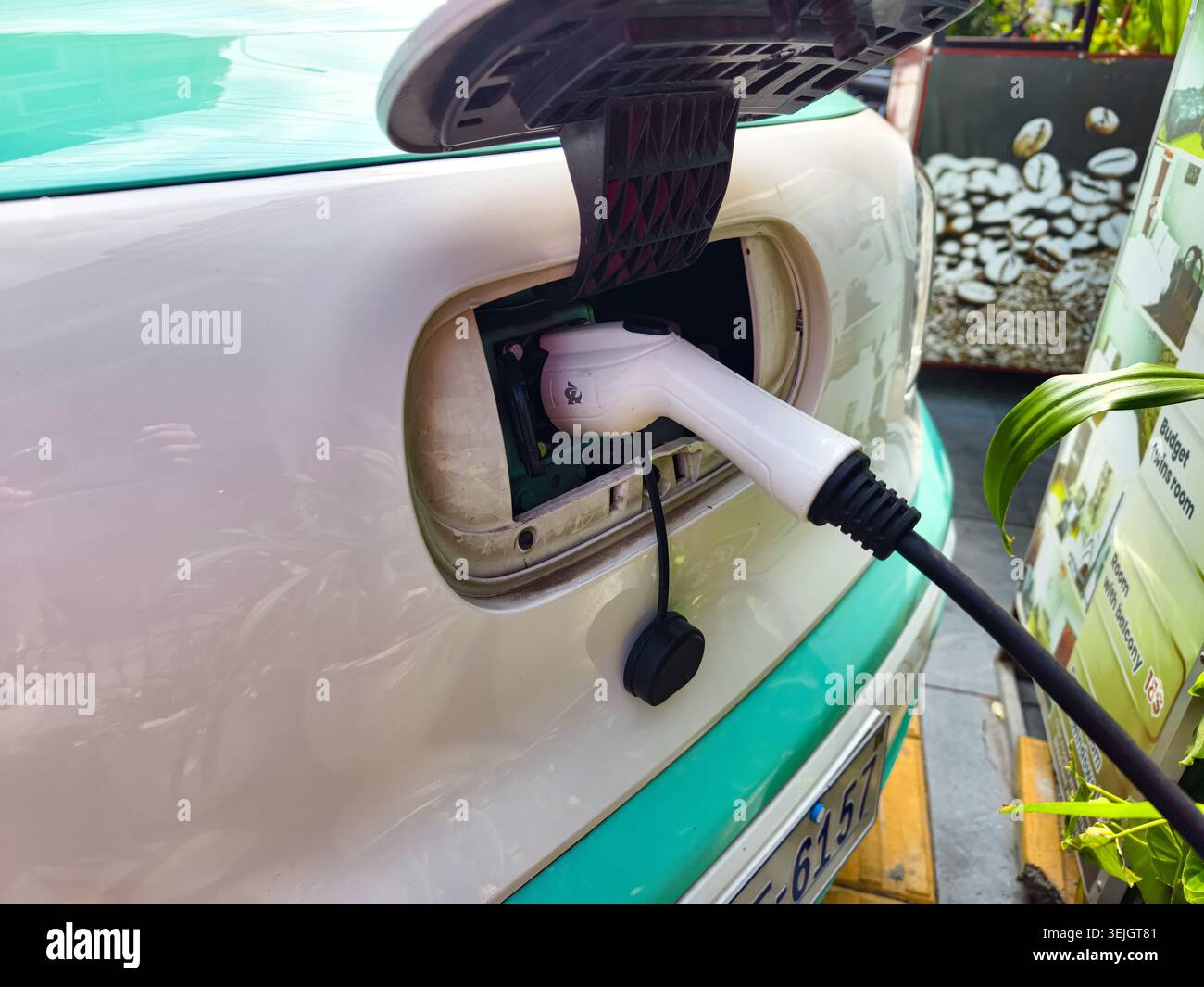 Ein Elektrofahrzeug mit zweifarbigem weiß-grünem Äußeren, das an ein Ladekabel angeschlossen ist. Phnom Penh, Kambodscha, Asien Stockfoto