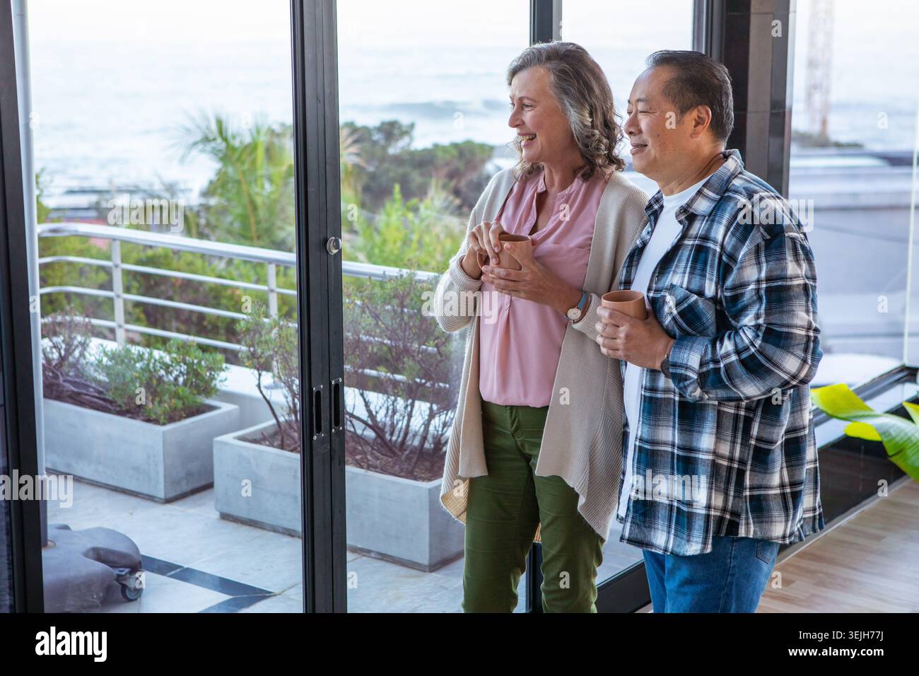 Verschiedene Seniorenpaare stehen an Glasschiebetüren auf dem Balkon und halten Tassen und beobachten das Meer. Gesellschaft, Freizeit, sereni Stockfoto