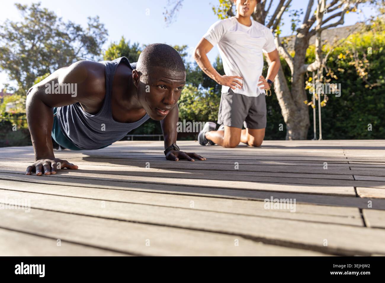 Diverse Männer-Duo in Sportbekleidung, die Liegestütze mit einem Coaching auf der Terrasse mit Fitness-Tracker durchführen. Fitness, Motivation, Outdoor Stockfoto