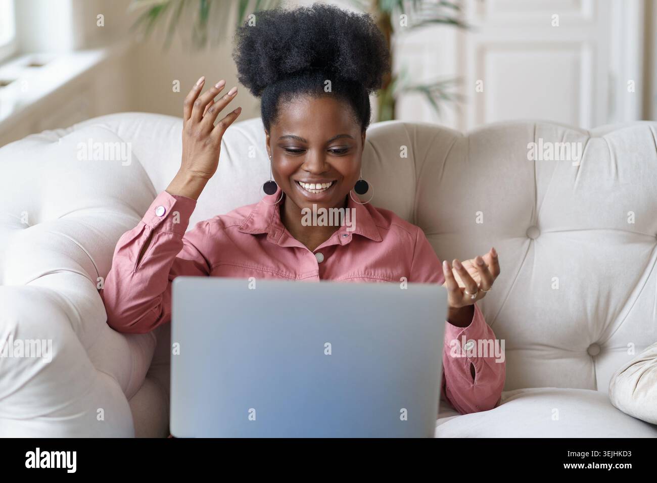 Lächelnde afrikanische junge Frau, die auf der Couch sitzt, auf die Kamera-Webcam schaut, lacht während des Schulungs-Webinars, spricht über V Stockfoto