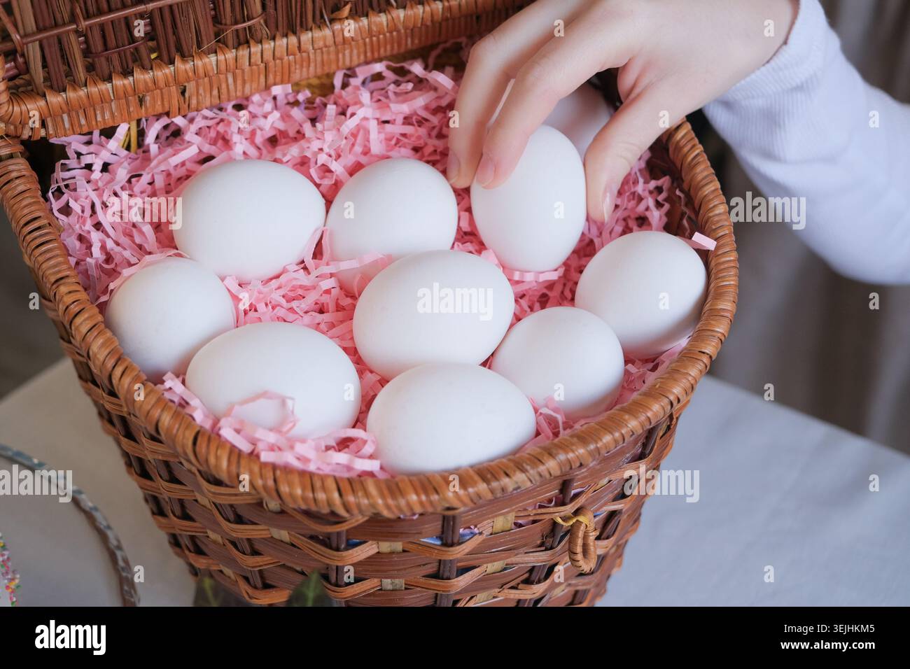 Unerkennbare Frau in Schürze, die weißen Eier in den Korb, bereit für Ostern, Eiermockup Stockfoto