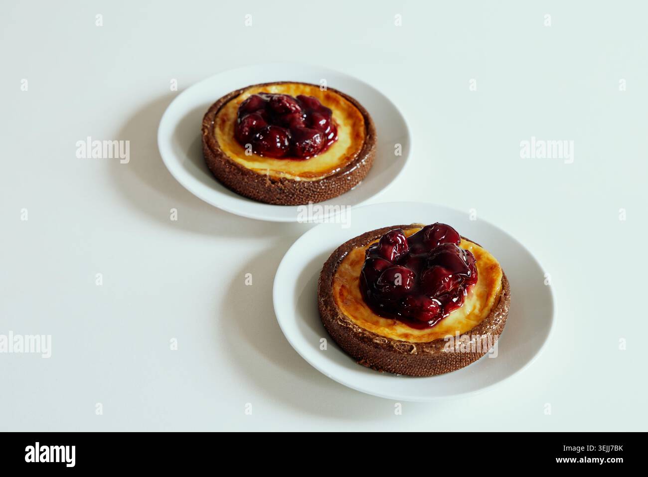 Zwei süße Kirschkäsekuchen mit roter Beerenmarmelade, serviert auf separaten weißen Keramikplatten auf einem sauberen Hintergrund. Stockfoto