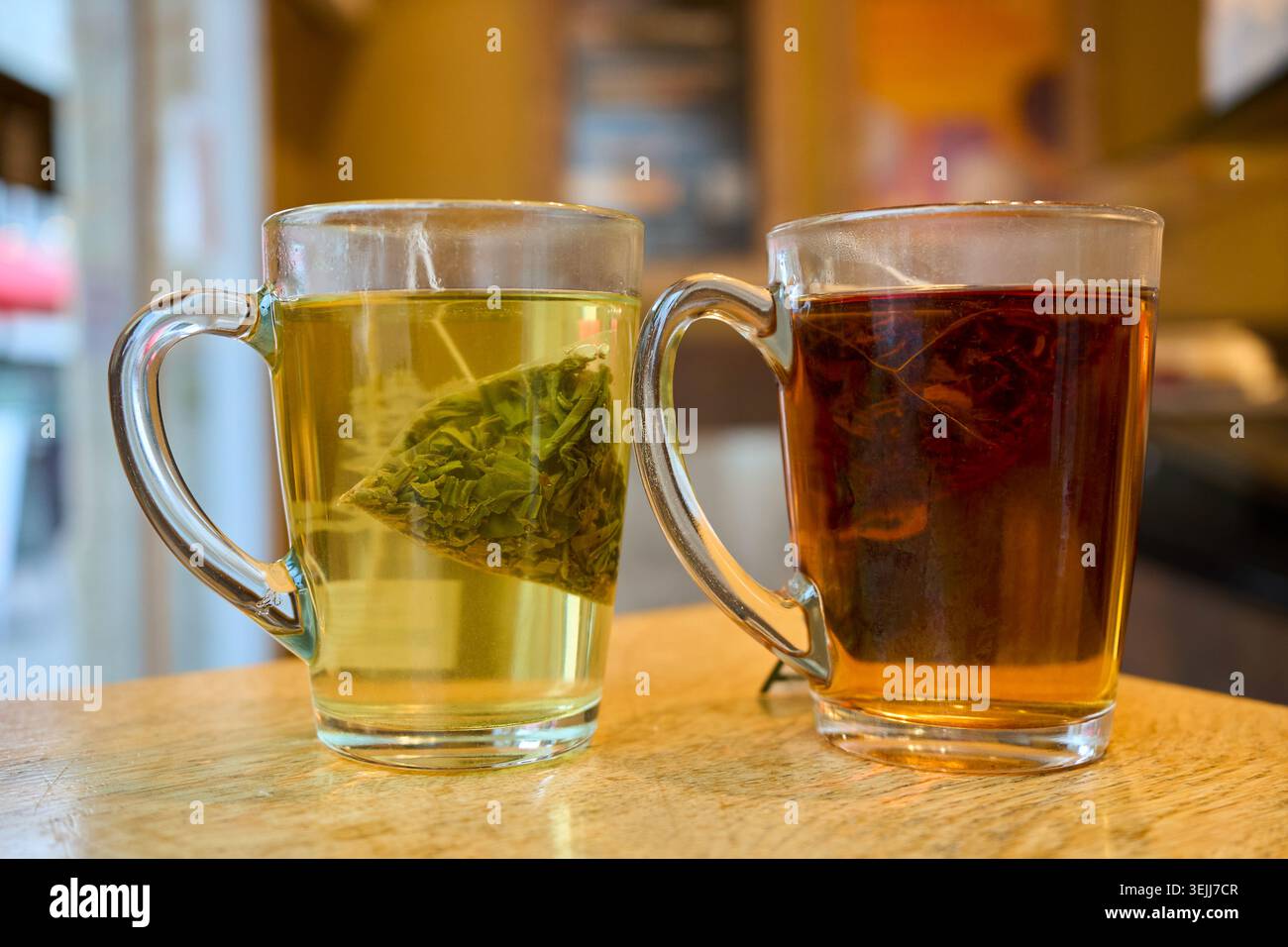 Zwei transparente Glasbecher mit grünem und schwarzem Tee aus Pyramiden-Teebeuteln, die auf einem Holztisch in einem Café stehen. Stockfoto