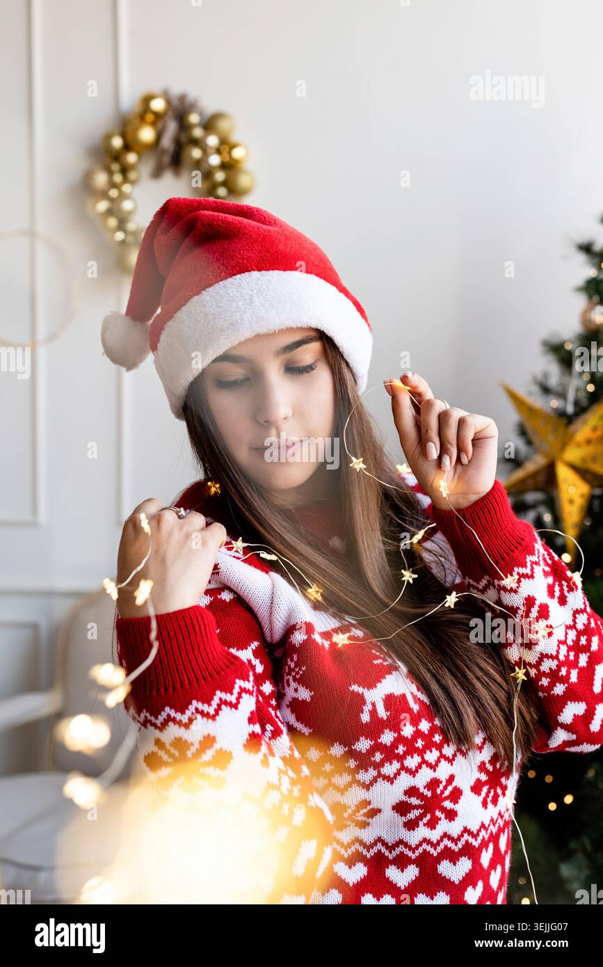 Eine junge Frau mit weihnachtsmütze und Pullover, die wunderschöne weihnachtslichter hält Stockfoto
