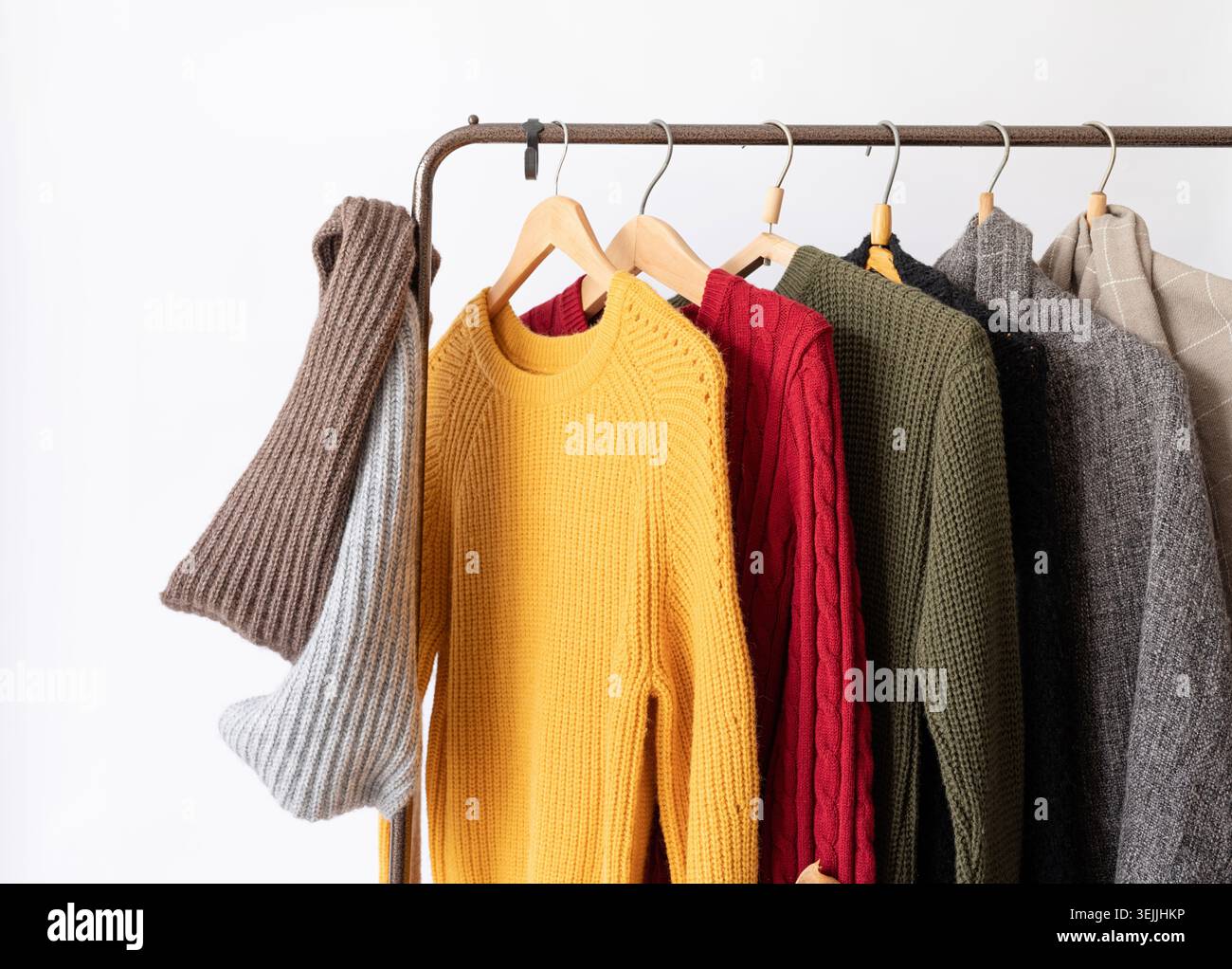 Eine Reihe verschiedener farbenfroher Strickpullover hängt an Kleiderbügeln, weißer Hintergrund Stockfoto